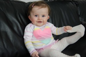 Ella Gavin (8mths) sits on the couch stretching her sock. Photo: Brad Roberts.