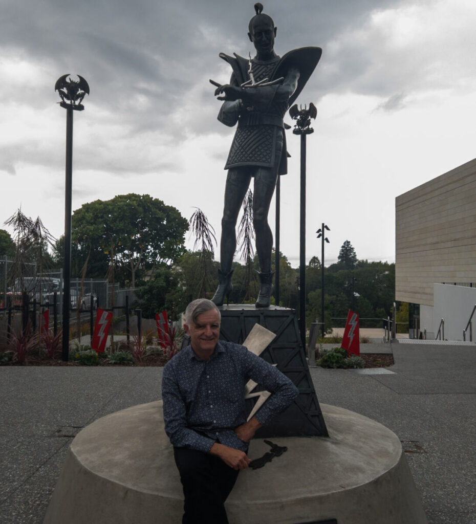 Mark Servian sitting in front of a statue of Riff Raff from the Rocky Horror Picture Show.